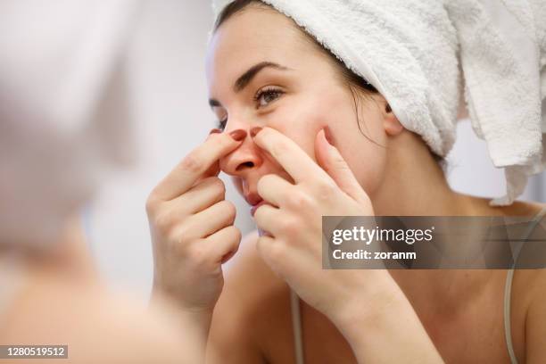 reflection of woman with towel on head squeezing blackhead on her nose side - human nose stock pictures, royalty-free photos & images