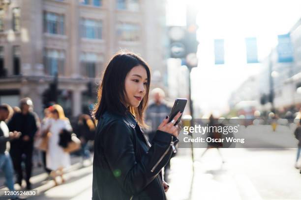 beautiful woman checking on mobile phone while crossing the street - daily life at oxford street london stock pictures, royalty-free photos & images