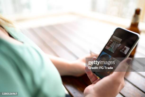 mujer bebiendo cerveza usando un teléfono inteligente para hacer una videollamada - plano fijo fotografías e imágenes de stock