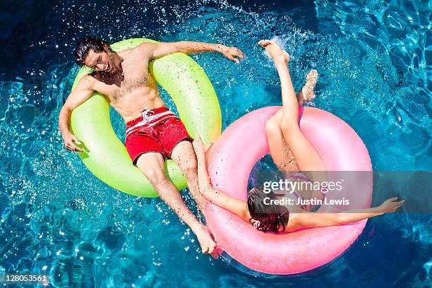 young couple playing around in pool on inner tubes - inner tube stock-fotos und bilder