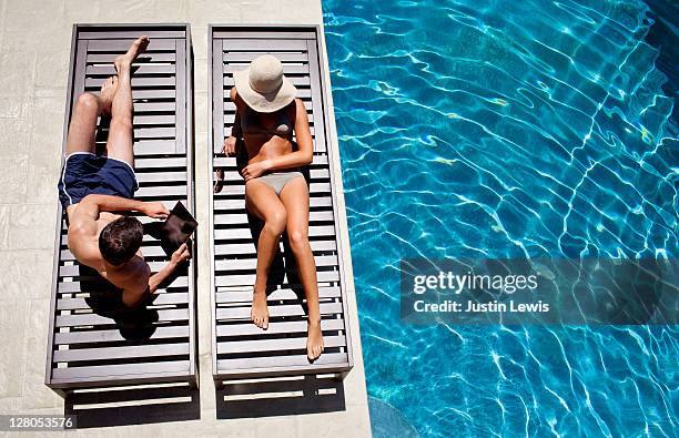 young couple on pool chairs next to luxury pool - man ipad holiday stockfoto's en -beelden