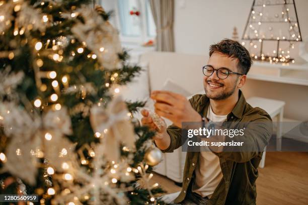 young man decorating christmass tree - decorating the christmas tree stock pictures, royalty-free photos & images