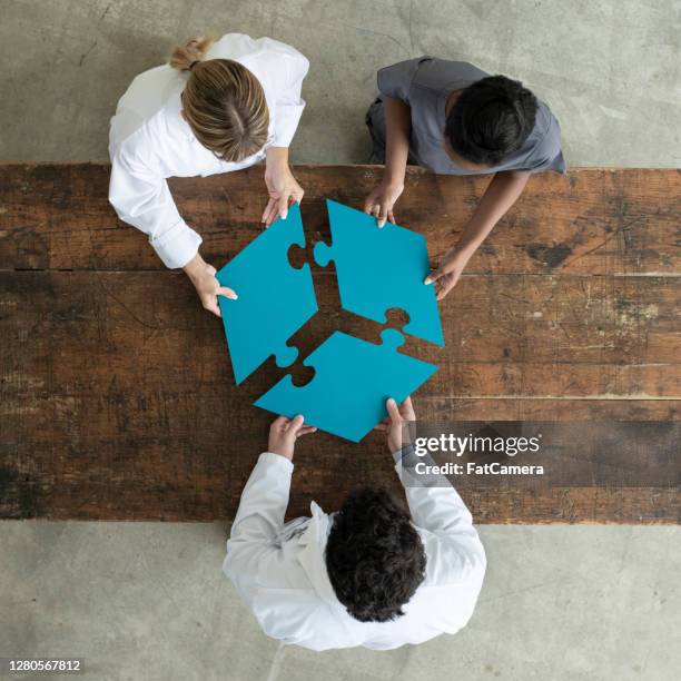 medical professionals putting a 3 piece puzzle together - three people at table stock pictures, royalty-free photos & images