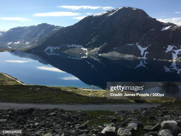 scenic view of lake by snowcapped mountains against sky, nibbevegen, geiranger, norway - james popple stock-fotos und bilder