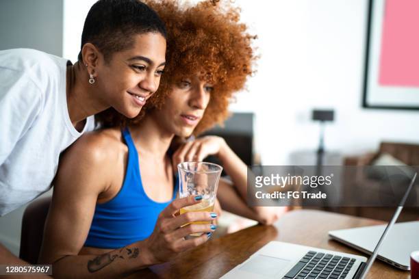 couple / friends doing a virtual happy hour at home or watching a video on laptop - transgender stock pictures, royalty-free photos & images