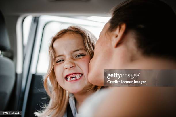 happy daughter kissed by mother looking at camera - auto küssen stock-fotos und bilder