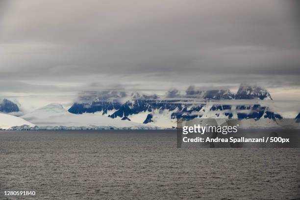 scenic view of sea by snowcapped mountains against sky, antarctica - ghiacciai stock-fotos und bilder