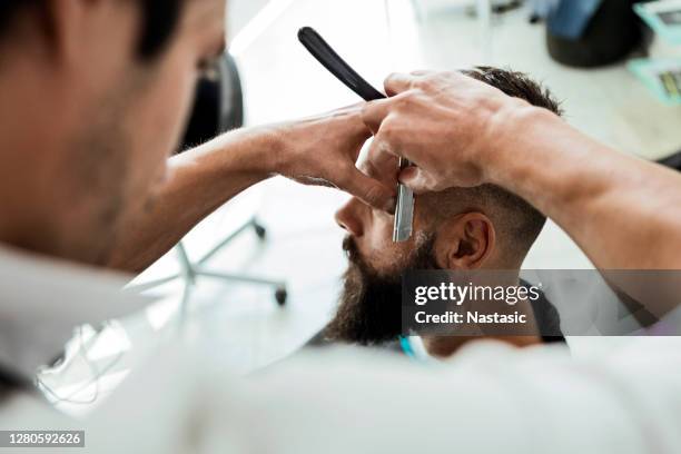 barber shaves the beard of the client - shave barber stock pictures, royalty-free photos & images