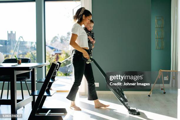 mother vacuum cleaning while carrying toddler son - cleaning equipment stock pictures, royalty-free photos & images