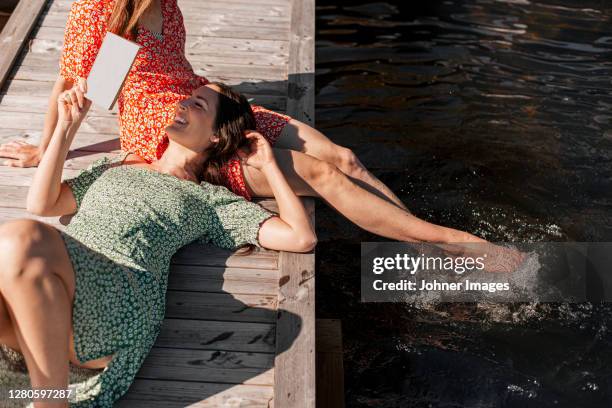 female friends relaxing on jetty - bootssteg stock-fotos und bilder