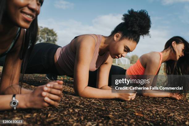 three woman in a sunny outdoor environment planking - yoga group stock-fotos und bilder