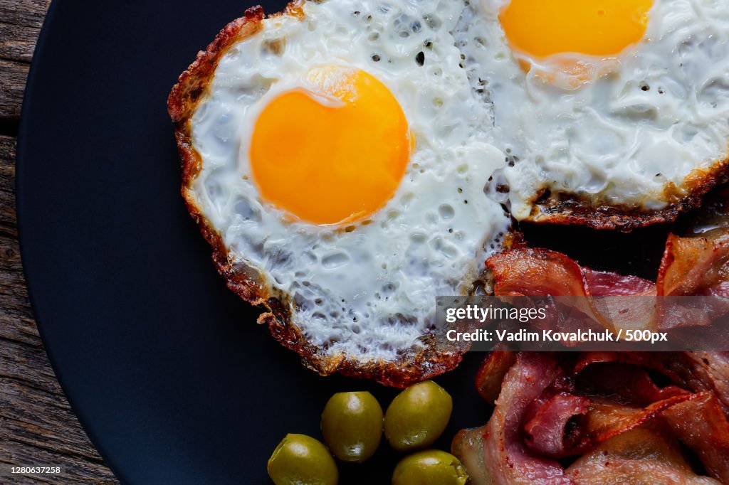 Fried eggs with bacon on a wood plate on a black background