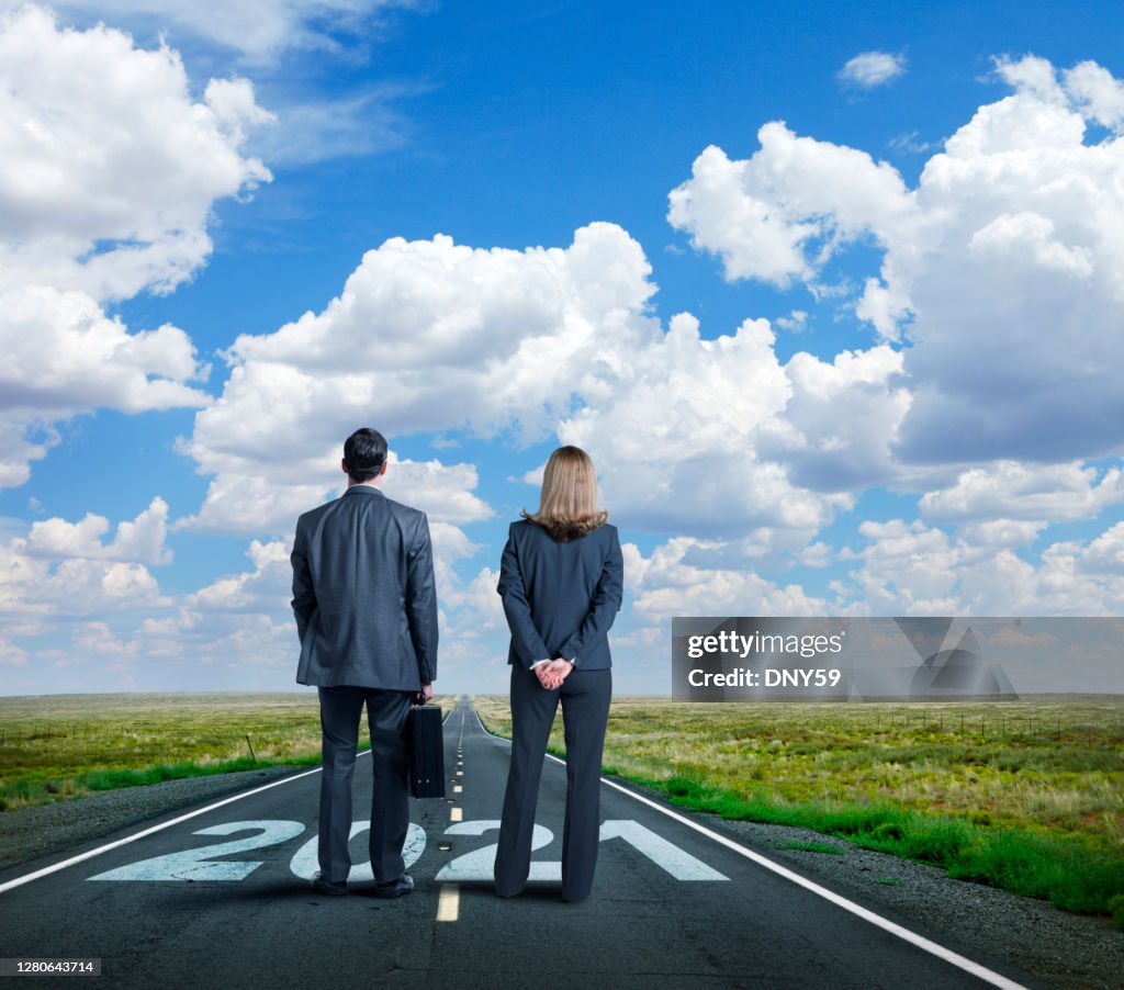 Businesswoman And Businessman Stand On Long Road With The Year 2021 Painted On It