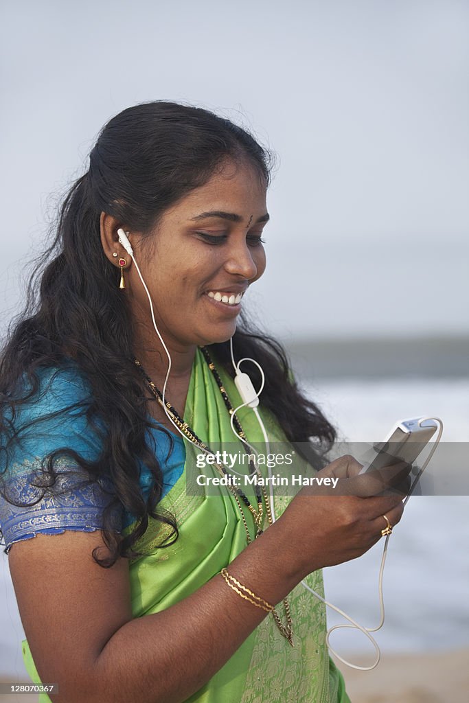Woman (28 years old) in traditional bright green and turquoise sari listening to an mp3 player on Marari beach Alappuzha, Kerala, India