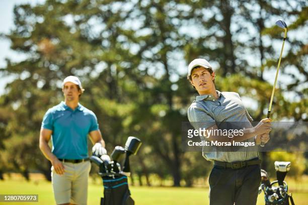 golfer teeing off while friend standing in golf course - play off stock pictures, royalty-free photos & images