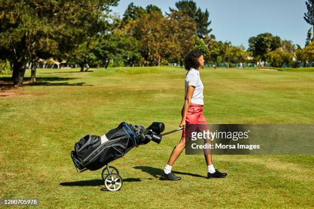 smiling female golfer with golf bag walking on grassy land - golf short iron stock pictures, royalty-free photos & images