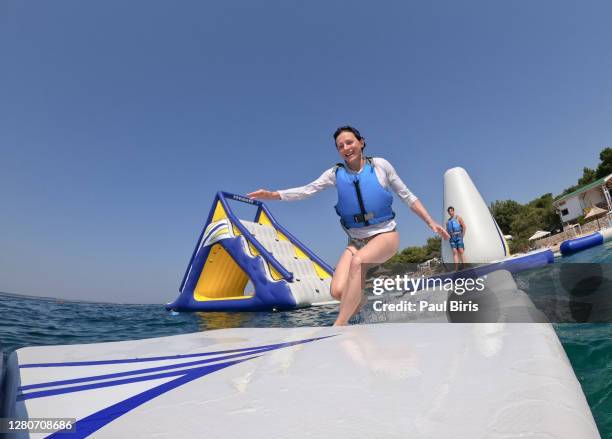young woman running on an inflatable playground on the beach on a summer day. - bouncy castle beach stock pictures, royalty-free photos & images