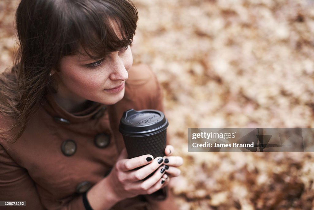 Young woman enjoying coffee amongst autumn leaves