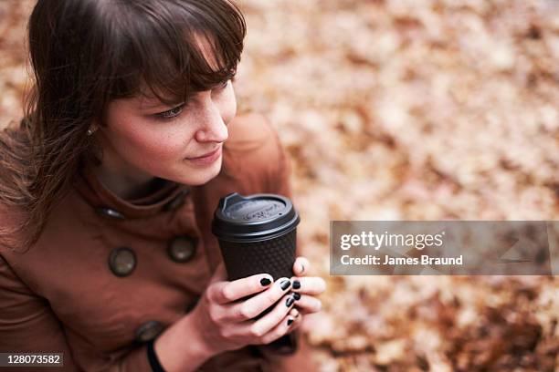 young woman enjoying coffee amongst autumn leaves - esmalte de uñas negro fotografías e imágenes de stock