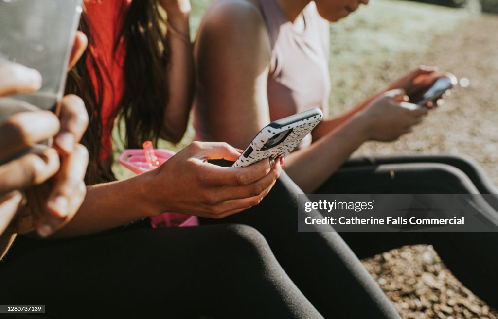 Three woman holding their mobile phones outside and looking at the screens