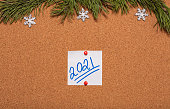White sticky note with 2021 handwritten on it pinned on notice board which is decorated with pine twigs and snowflakes. 2021 Christmas, new years celebration season concept.