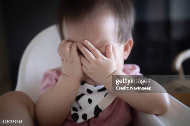 cute asian baby with bib, distress on high chair, hands over face - baby pout stock pictures, royalty-free photos & images
