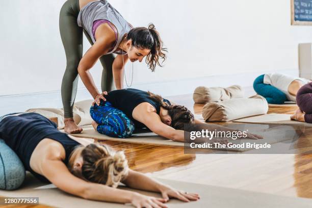 trainer assisting woman in doing child's pose at yoga class - yoga instructor stock pictures, royalty-free photos & images