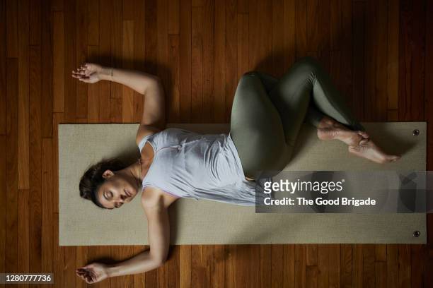 directly above shot of relaxed young woman doing yoga on exercise mat in studio - acostado fotografías e imágenes de stock