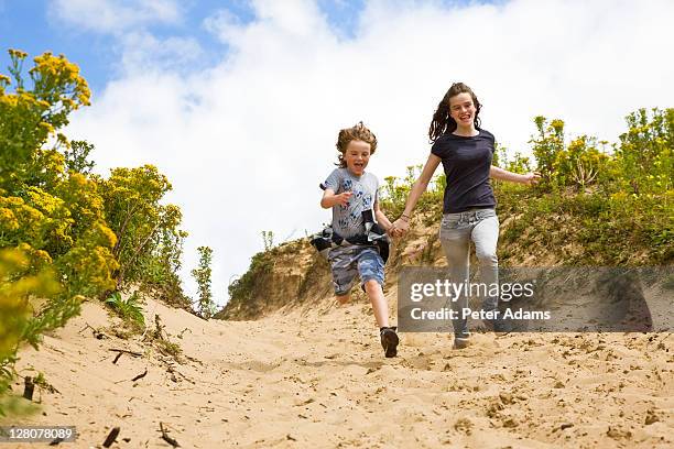 brother, 9 years old and sister, 15 years old, running down sand dunes, s. wales, uk - 14 15 years fotografías e imágenes de stock