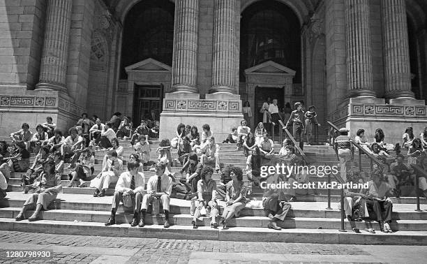 View of people seated on the steps outside the New York Public Library Main Branch during lunch hour , New York, New York, June 26, 1979.