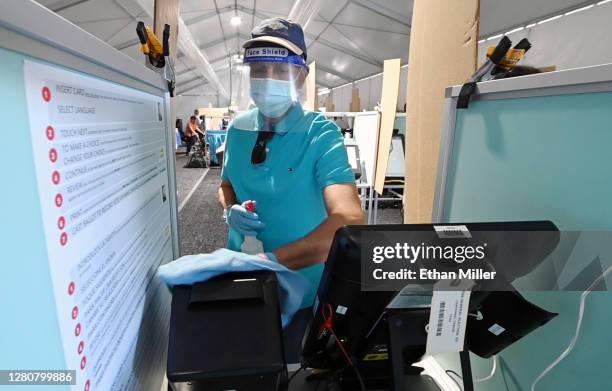 Carl Chamberlain sanitizes a voting booth between voters inside a tent at a shopping center on the first day of in-person early voting on October 17,...