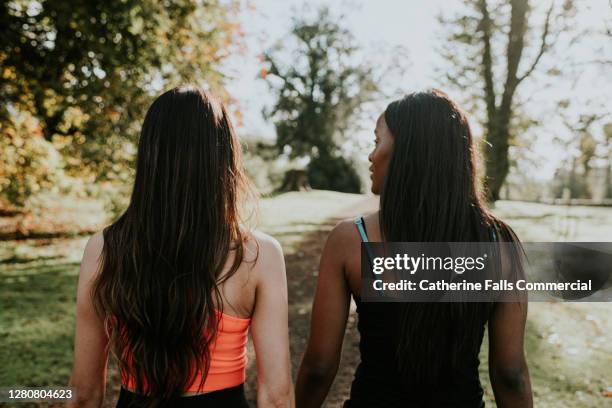 two young woman walking through a sunny park - annual woman stockfoto's en -beelden