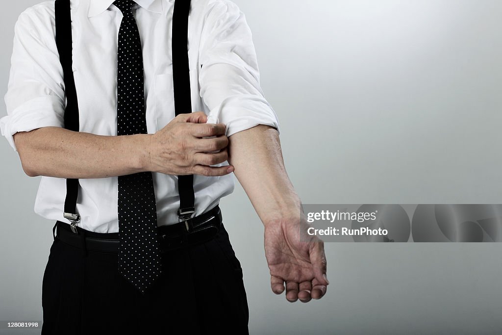 Old age businessman turning up cuff on shirt