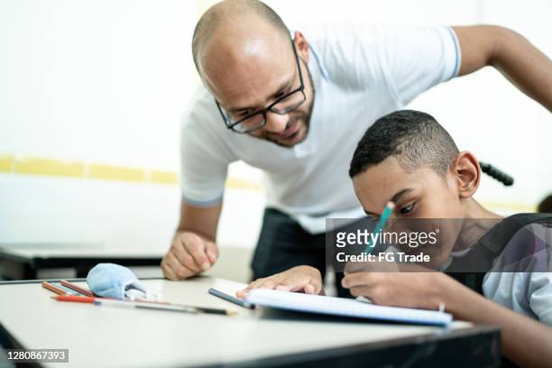 male teacher helping student with disability in the classroom - private school uniform stock pictures, royalty-free photos & images