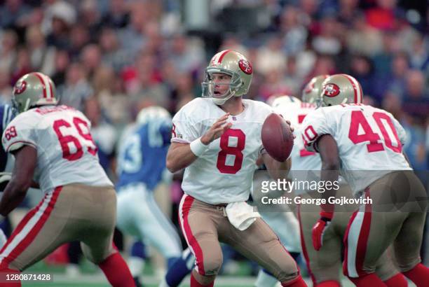 Quarterback Steve Young of the San Francisco 49ers looks to pass as offensive lineman Rod Milstead and running back William Floyd block during a game...
