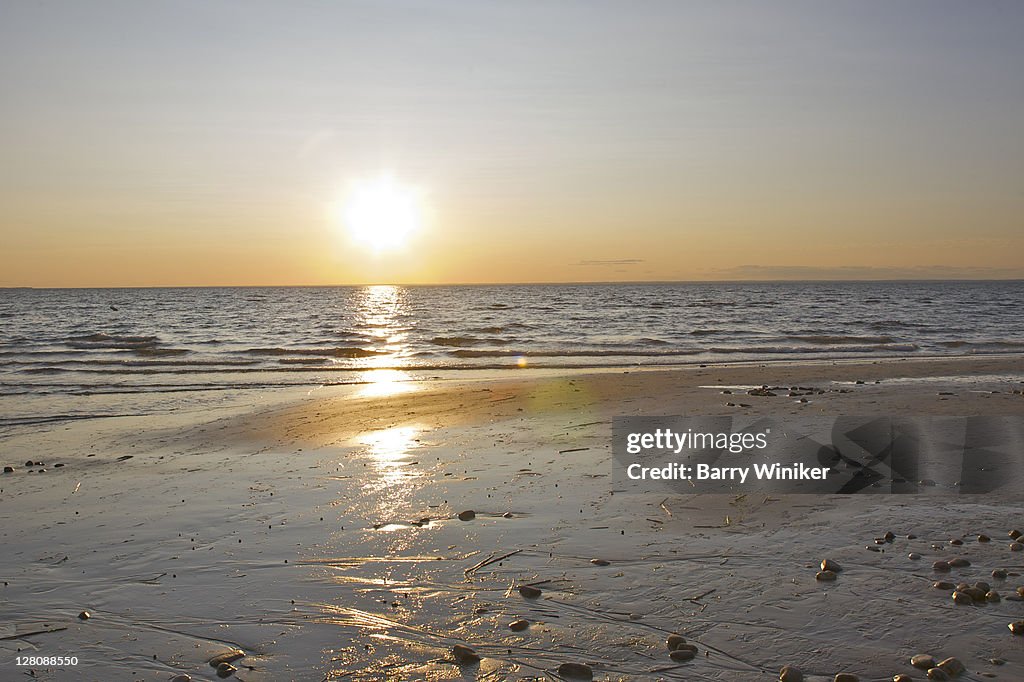 Sun low in sky, reflecting in water and shoreline, West Meadow Beach at dusk, Stony Brook, NY, U.S.A.