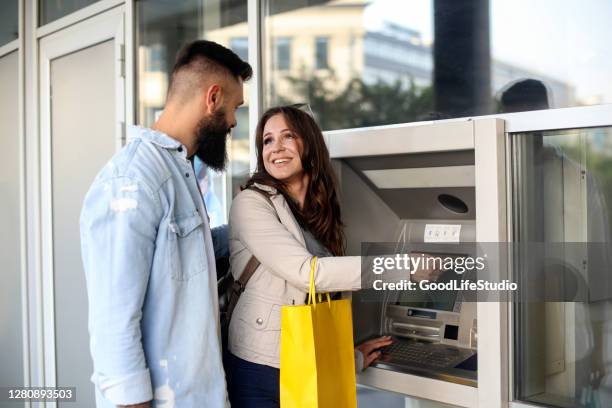 young couple using an atm - man atm smile stock pictures, royalty-free photos & images