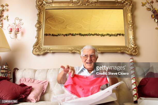 senior man holding up pink panties - funny dressed man stock-fotos und bilder