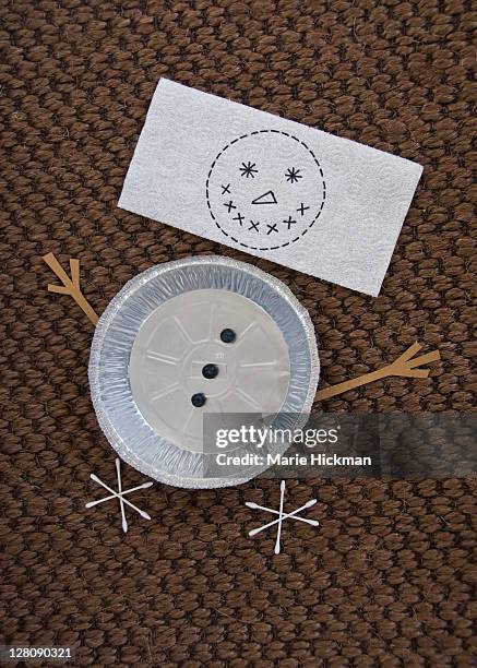 snowman made up of a tin pie pan and drawing of a face on a paper towel, and cotton swabs as feet on a dark-brown woven rug - brown paper towel stock pictures, royalty-free photos & images