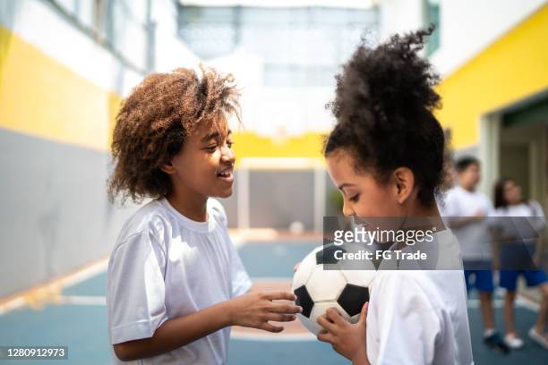 grundschüler halten einen fußball auf dem sportplatz - brazilian playing football stock-fotos und bilder