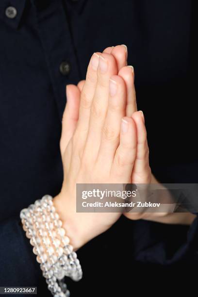 transparent crystal rosary on the hand of a young woman. the girl's hands are folded in a prayer gesture. religious symbol of the concept of faith, prayer, meditation, and mantra repetition. - chant stock pictures, royalty-free photos & images