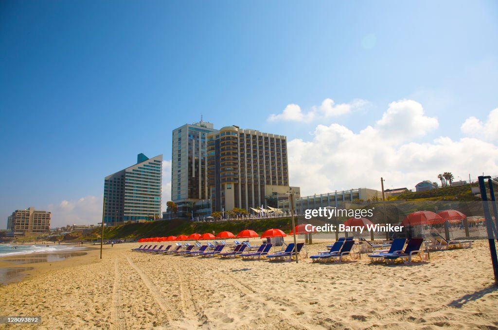 Beach chairs, umbrellas and residential and hotel towers on beach in Herzliya, Israel