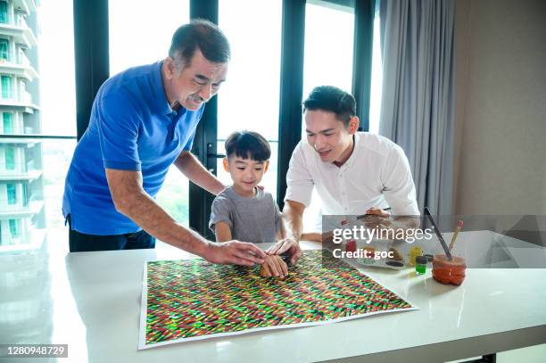 grandson picked up batik printing skill from his grandpa and dad by using fresh potato and paint color. grandpa use a cut potato as batik stamp and apply color paint on to it and make the seamless pattern design on paper. - batik painting stock pictures, royalty-free photos & images