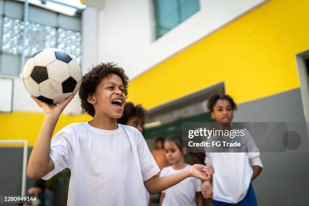 schoolboy shouting and about to throw a soccer ball on exercising class at school - sports centre exterior stock pictures, royalty-free photos & images