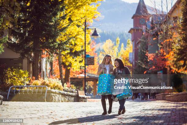 dos mujeres caminando por el pueblo de whistler con bolsas de compras. - localidad pequeña fotografías e imágenes de stock