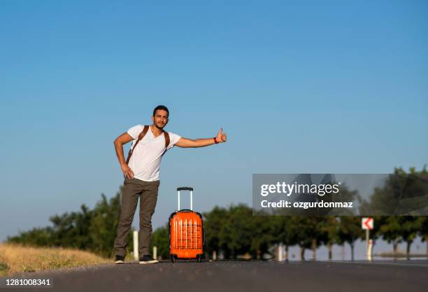 joven viajero haciendo autostop en la carretera - hitchhiking fotografías e imágenes de stock