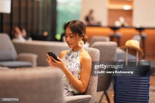 asian woman sitting at airport terminal lounge and using phone to chatting - embarquement photos et images de collection
