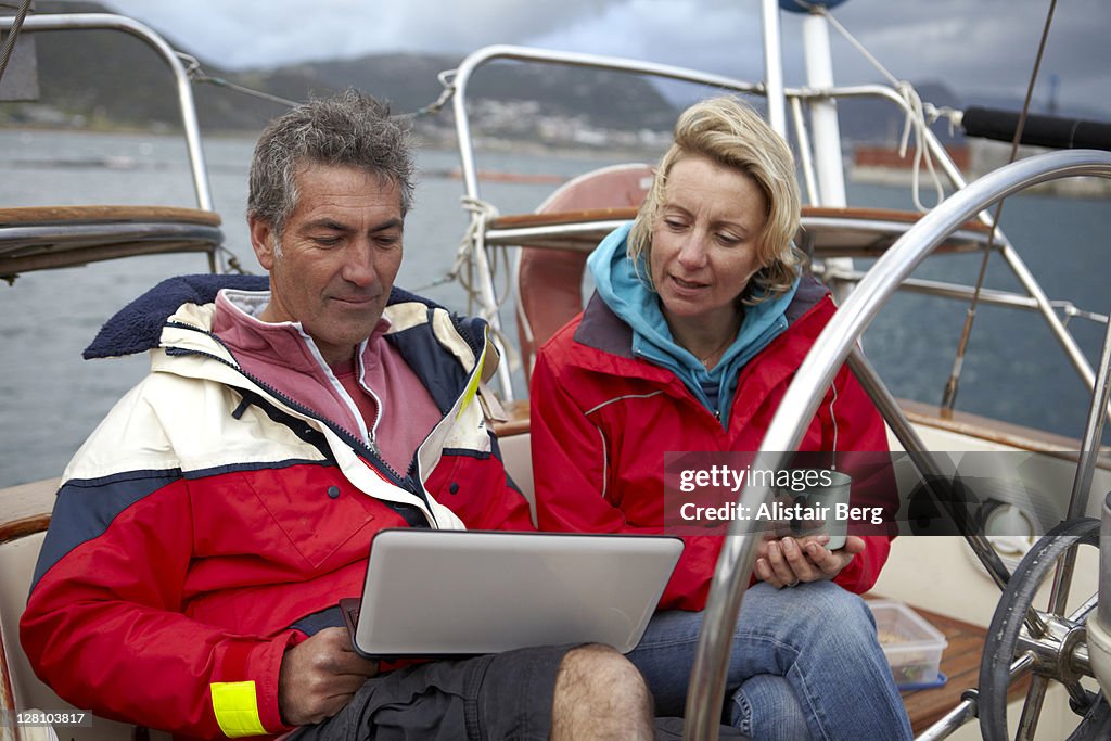 Couple using computer while sailing