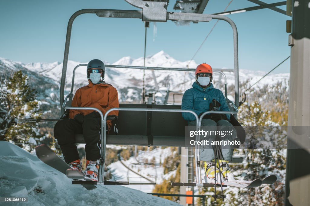 Two skiers with mouth nose mask on chair lift