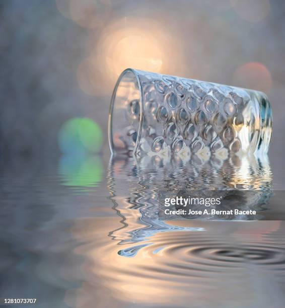 impact of a glass of crystal with water that falls down reflected in the water. - broken cup stock-fotos und bilder